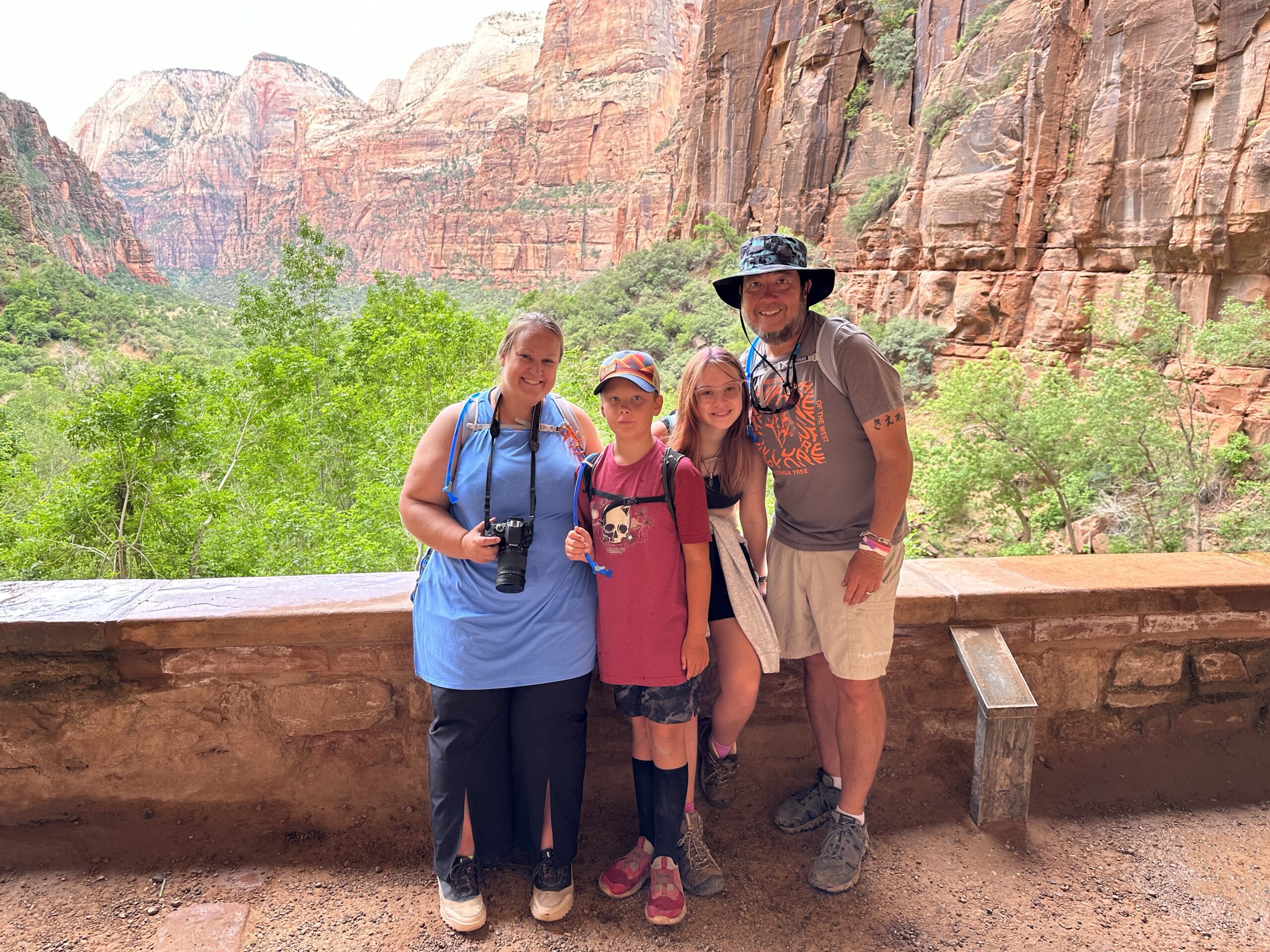 Family standing at the Weeping Gardens in Zion National Park with Red Mountains and trees in the background