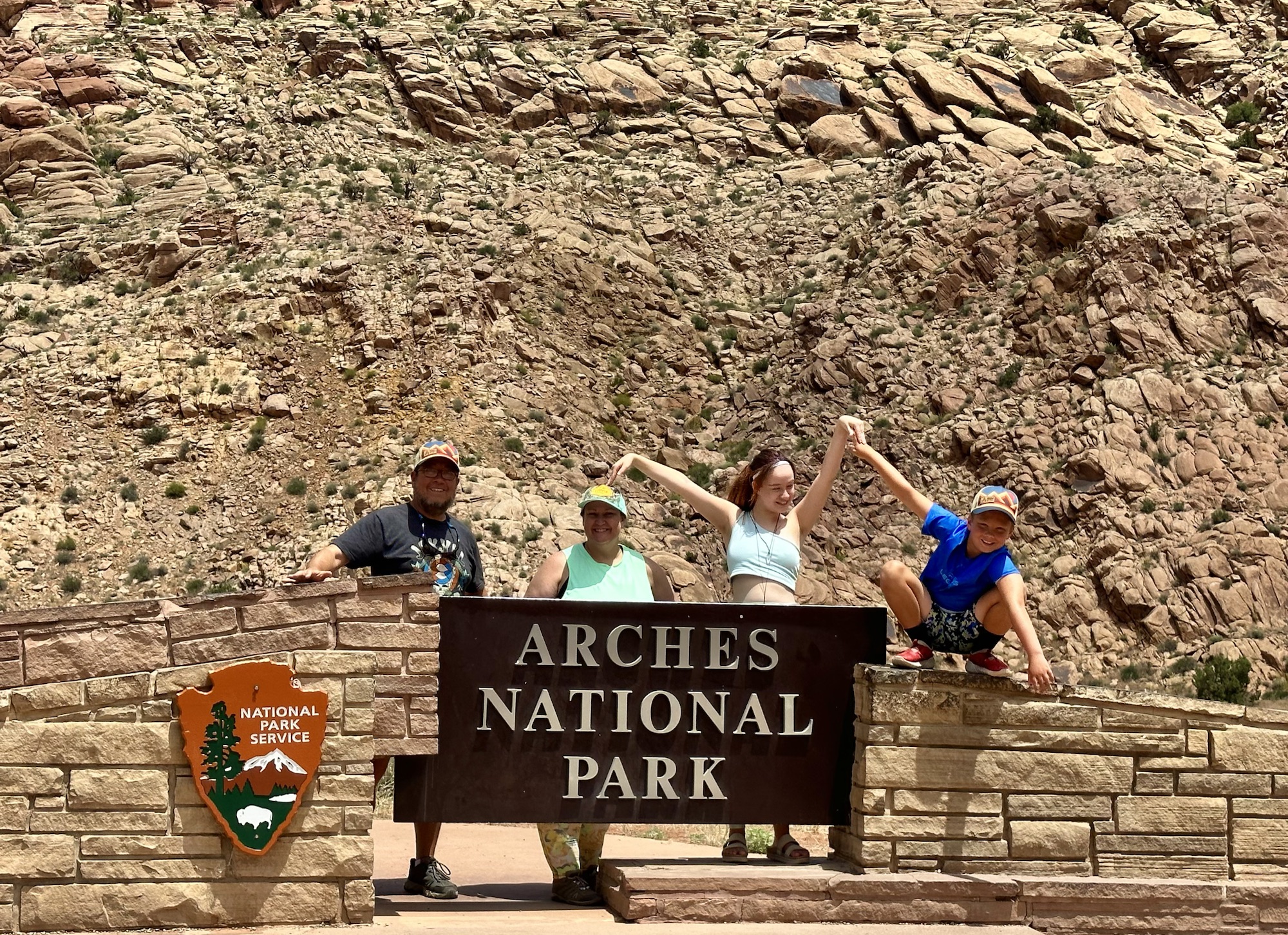 Family poses by the entrance sign to Arches National PArk
