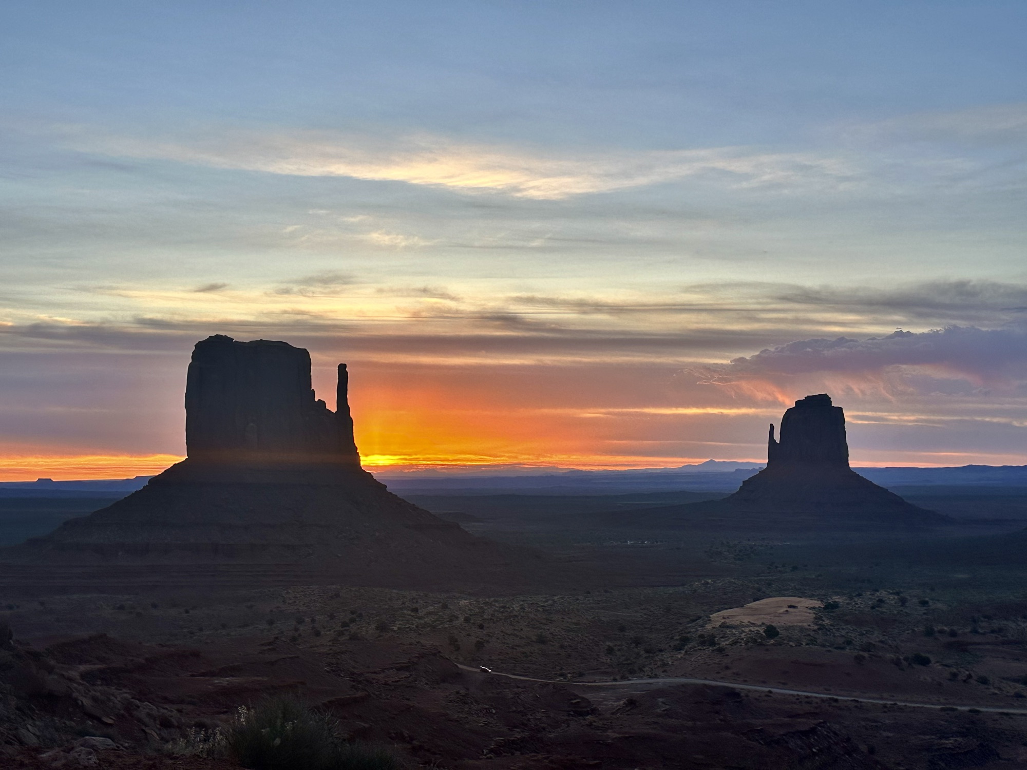 Sun rises up behind sandstone buttes in Monument Valley